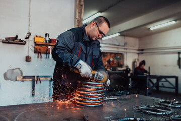 Locksmith in special clothes and goggles works in production. Metal processing with angle grinder. Sparks in metalworking.