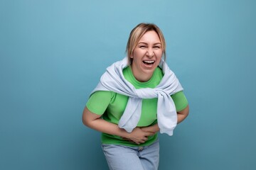 blond cheerful bright girl in a casual outfit laughing widely until her stomach hurts on a blue background with copy space