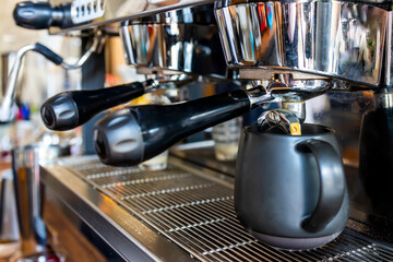 Coffee machine pouring coffee in black cup. Selective focus with group head or portafilter with blur background.Close up photo in coffee shop.Espresso pouring from engine.Professional coffee brewing.