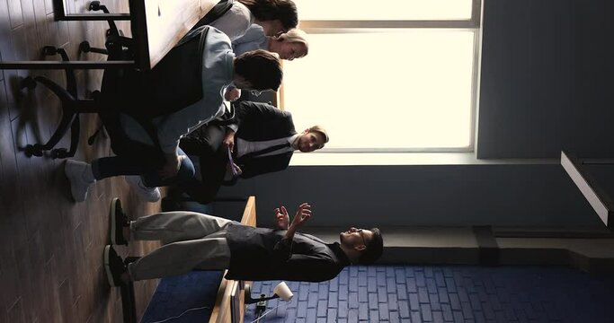Business leader man talking to employees on team meeting, speaking to audience, explaining work tasks, project plan, strategy, standing before row of colleagues sitting on chair. Vertical shot