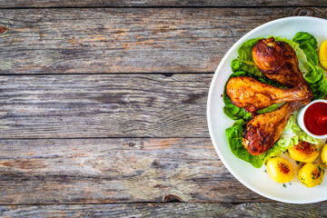 Barbecue chicken drumsticks with fried potatoes, lettuce and ketchup on wooden table
