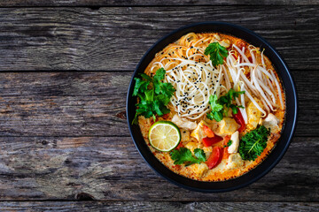 Tom Kha - Thai soup with chicken breast nuggets and noodles on wooden table
