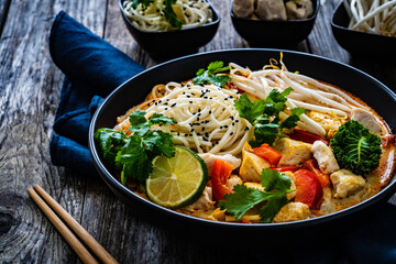 Tom Kha - Thai soup with chicken breast nuggets and noodles on wooden table
