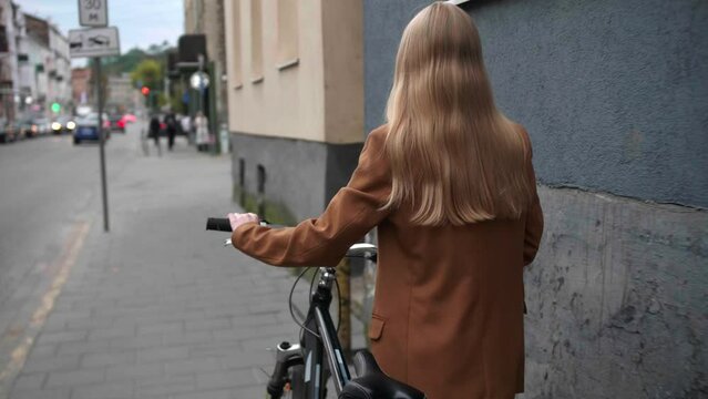 Young woman with bicycle walking on street, back view. Camera moving forward after her, slow motion effect