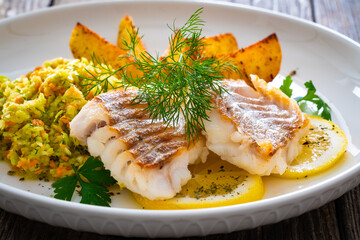 Fish dish - fried cod with baked potatoes and fresh vegetables on wooden table
