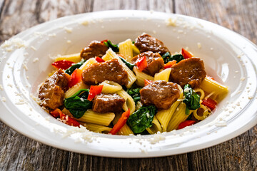 Pasta with roasted pork loin, spinach and parmesan on wooden table
