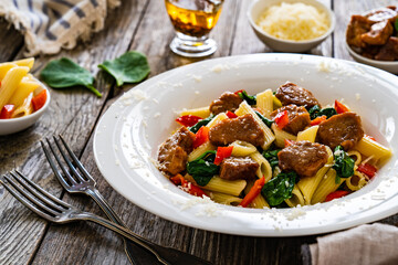 Pasta with roasted pork loin, spinach and parmesan on wooden table
