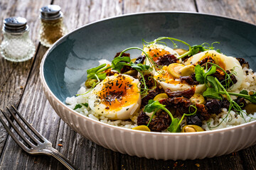Boiled eggs with boiled white rice, sun dried tomatoes  and green olives on wooden table