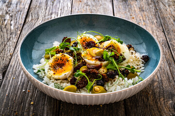Boiled eggs with boiled white rice, sun dried tomatoes  and green olives on wooden table