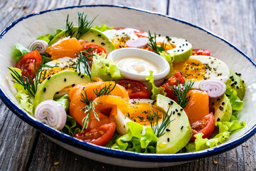 Salmon salad - smoked salmon, hard boiled eggs, avocado and leafy greens on wooden table
