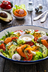 Salmon salad - smoked salmon, hard boiled eggs, avocado and leafy greens on wooden table

