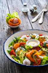 Salmon salad - smoked salmon, hard boiled eggs, avocado and leafy greens on wooden table

