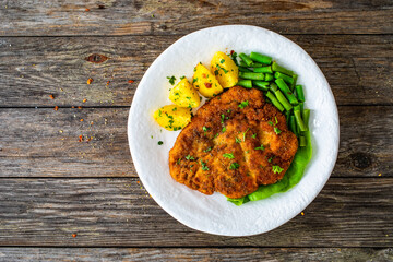 Breaded fried pork chop with green beans and potatoes on wooden table
