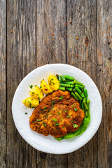 Breaded fried pork chop with green beans and potatoes on wooden table
