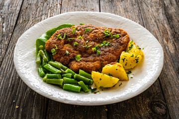 Breaded fried pork chop with green beans and potatoes on wooden table
