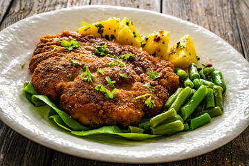 Breaded fried pork chop with green beans and potatoes on wooden table
