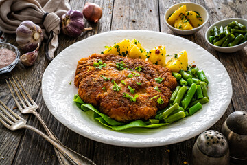 Breaded fried pork chop with green beans and potatoes on wooden table
