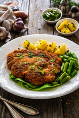 Breaded fried pork chop with green beans and potatoes on wooden table
