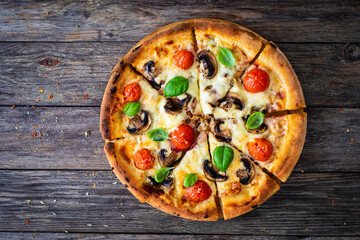 Circle vegetarian pizza with mozzarella cheese, mushrooms and tomatoes on wooden table
