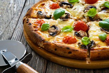 Circle vegetarian pizza with mozzarella cheese, mushrooms and tomatoes on wooden table
