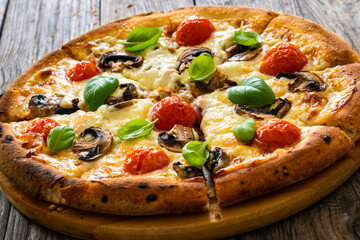 Circle vegetarian pizza with mozzarella cheese, mushrooms and tomatoes on wooden table
