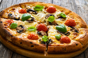 Circle vegetarian pizza with mozzarella cheese, mushrooms and tomatoes on wooden table
