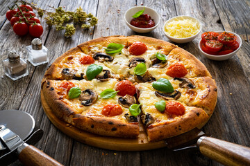 Circle vegetarian pizza with mozzarella cheese, mushrooms and tomatoes on wooden table
