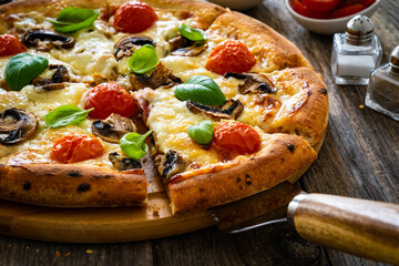 Circle vegetarian pizza with mozzarella cheese, mushrooms and tomatoes on wooden table

