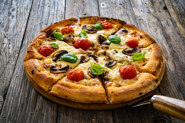 Circle vegetarian pizza with mozzarella cheese, mushrooms and tomatoes on wooden table
