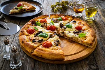 Circle vegetarian pizza with mozzarella cheese, mushrooms and tomatoes on wooden table

