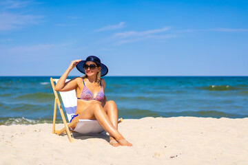 Fototapeta na wymiar Woman relaxing on beach sitting on sunbed 