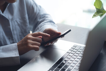 Business woman sitting at office table using mobile phone while online working on laptop computer...