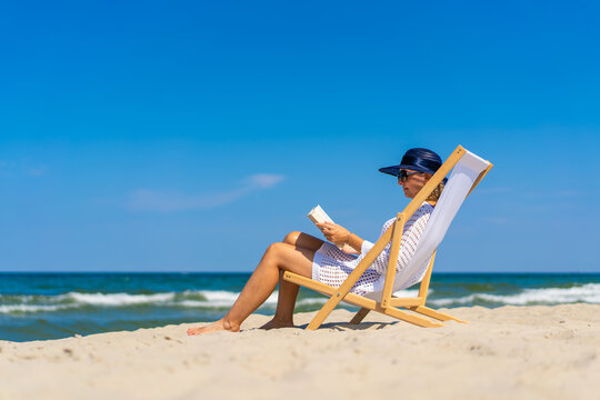 Woman relaxing on beach reading book sitting on sunbed
