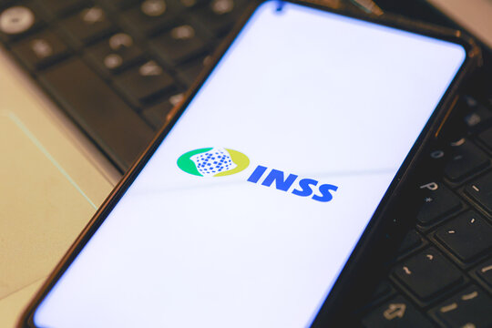 A logo do INSS na tela de um telefone celular que est&aacute; sobre um teclado de um laptop. Instituto Nacional do Seguro Social.