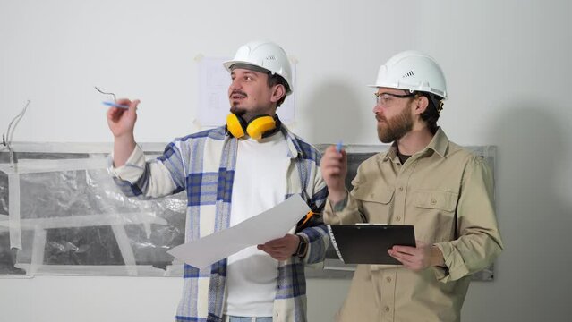 An architect and a construction engineer are standing at a construction site with documents in their hands and discussing the details of the project and the work plan for the day. High quality 4k