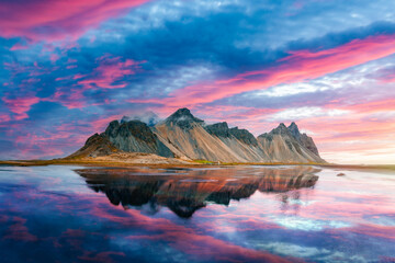 Incredible Stokksnes mountains on Vestrahorn cape in southeastern Icelandic coast during sunset. The epic pink sky reflected in the clear water. Iceland island. Landscape photography - obrazy, fototapety, plakaty