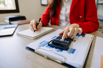 Fototapeta premium Women counting coins on calculator taking from the piggy bank. hand holding pen working on calculator to calculate on desk about cost at home office.