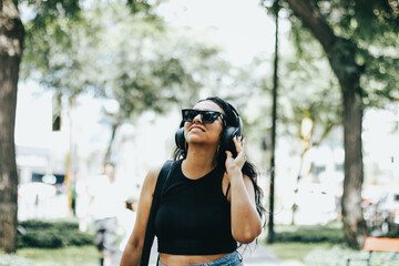 Photo of a woman listening to music with wireless headphones while wearing sunglasses. Lifestyle concept.