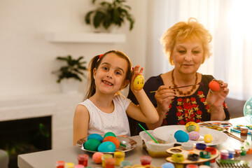 Obraz na płótnie Canvas Little girl and her grandmother painting Easter eggs at home.