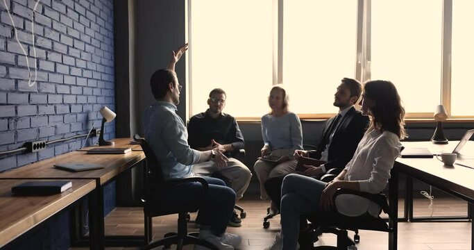 Serious group leader man speaking on teambuilding meeting. Business team sitting on chairs in circle, talking, discussing project ideas, brainstorming, listening to male boss