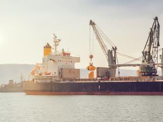 grain deal 2023. Close up Bunkering of dry cargo ship with grain at sunset golden hour. Loading with harbor crane 