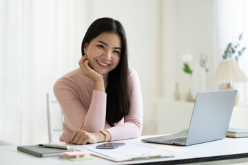 Portrait of young attractive Asian businesswoman smiling to the camera while sitting at her desk.