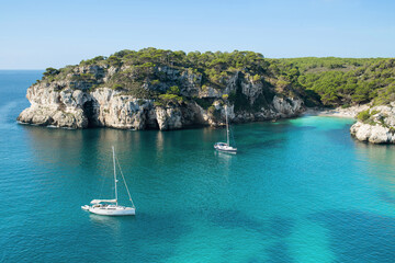 Beautiful beach with sailing boat yacht, Menorca island, Spain. Sailing boats in a bay. Summer fun, enjoying life, yachting, travel and active lifestyle concept - obrazy, fototapety, plakaty