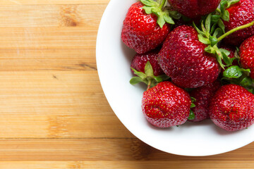 Large, red strawberries lie in a white plate on a wooden surface.