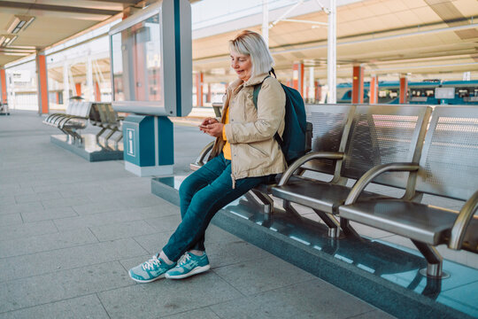 Old happy woman with backpack in yellow hat checking her ticket on background train. Railroad transport concept. Railroad transport concept. High quality photo