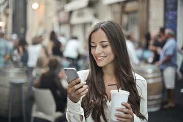 young woman drinks a soft drink in a cafe and uses a smartphone