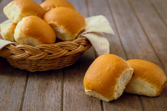 Soft bread rolls on wooden table and wicker basket