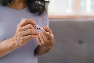 Close-up of a senior woman's hand checking her blood sugar level with a glucometer by herself at her home.