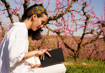 woman reading a book in a field of pink peach blossoms in spring. World day of the book. Sant Jordi