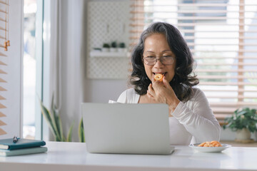 Capturing the Joys of Aging: A Happy Senior Woman Embracing Technology as She Navigates Her laptop computer with Ease from the Comfort of Her Home.